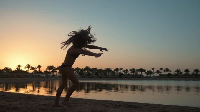 Smiling young woman showing cartwheel on sea coastline at sunset time.