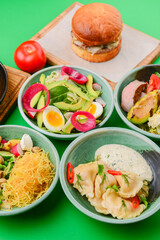 Variety of food dishes on bright green background. Table covere with food flat lay, top view, frame.