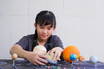 Selective focus at young Asian girl making homemade solar system model on wooden table at home for...
