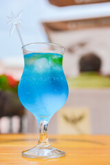 Blue curacao cocktail in a tall glass with a plastic straw outside. Delicious dessert drink, refreshing summer beverage.