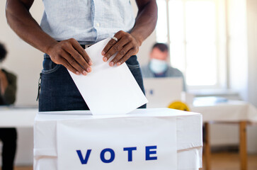 Unrecognizable african-american man putting his vote in the ballot box, usa elections and...
