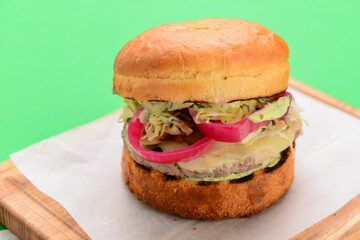 Home made burger on wooden tray over white table cloth and bright green background. Junk food, fast food concept.