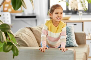 people and childhood concept - happy smiling little girl on sofa at home