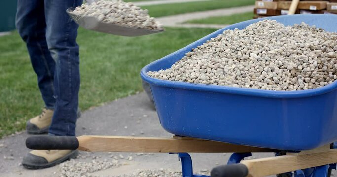 Man loads wheelbarrow with small stones - slow motion