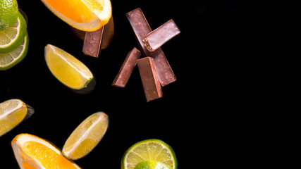 Fresh lemon lime orange slices with chocolate pieces on a black background top view