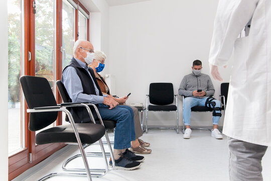 Senior couple with face masks sitting in a waiting room of a hospital together with a young man