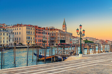 Fototapeta na wymiar Venice evening view with Fondamenta Salute embankment promenade near pier of Grand Canal waterway at sunset, Campanile bell tower and row of baroque style buildings in San Marco sestiere, Italy