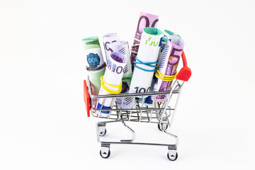 Close-up of a shopping cart full of euro and dollar bills, isolated on a white background. The...