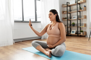 sport and people concept - happy smiling pregnant woman with smartphone exercising at home