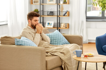 health, cold and people concept - sick young man in blanket with hot tea, lemon and honey on table at home