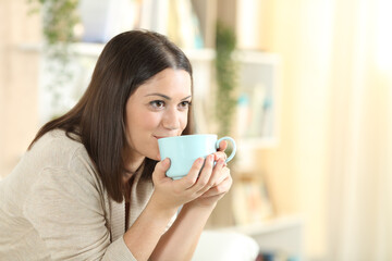 Happy woman drinking coffee sitting on a sofa at home