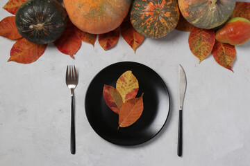 Table setting on Thanksgiving Day decorated pumpkin, pears and colorful leaves on grey. Top view