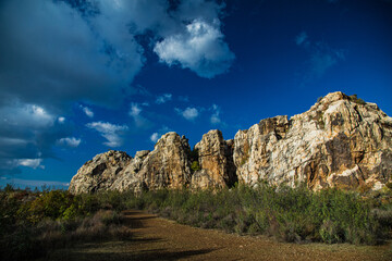 Colinas de rocas graníticas con maleza y tierra rojiza y cielo con nubes