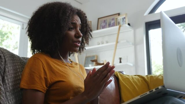 Beautiful girl wearing earphones chatting on video call with class mates sitting on sofa in lounge.