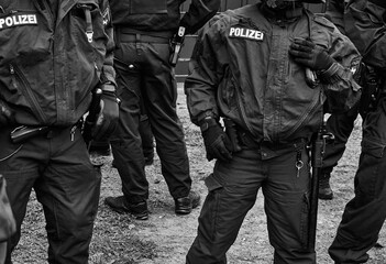 Policemen in black uniforms with pistols, handcuffs and batons, black and white, inscription Pollizei translates Police