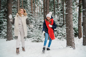 A young teenage girl plays snowballs with her beautiful mother in the winter in the park.