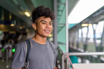 Happy young Asian tourist man as backpacker thinking at the sky train station