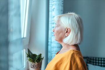 Sad caucasian woman 50 years old looks out the window. Hope concept. Concept home quarantine, prevention COVID-19, Coronavirus