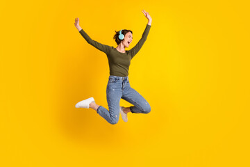 Full size photo of crazy excited girl jump listen wireless headset isolated over bright yellow color background