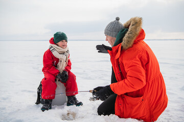 An experienced fisherman father teaches his young son to handle gear for winter fishing, they made a hole and fish in it