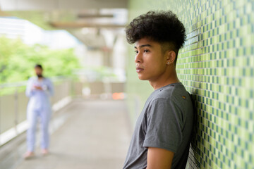 Profile view of young Asian man with curly hair at footbridge in the city