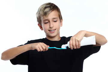 boy in white t-shirt squeezes toothpaste on brush and prepares to brush his teeth.