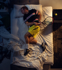 In love. Top view of young professional tennis player sleeping at his bedroom in sportwear with racket. Loving his sport even more than comfort, watching match even if resting. Action, motion, humor.