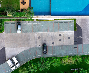 Top view concrete car parking lot, swimming pool, and garden of apartment. Aerial view of car parked at car parking area of condo. Outdoor parking space with empty slot. One way traffic sign on road.