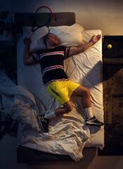 In love. Top view of young professional tennis player sleeping at his bedroom in sportwear with racket. Loving his sport even more than comfort, watching match even if resting. Action, motion, humor.
