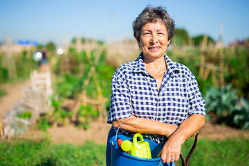 Portrait of positive elderly female gardener posing in backyard garden on sunny day