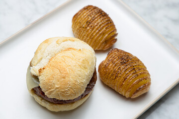 Homemade cheeseburger with hasselback potatoes on a white plate