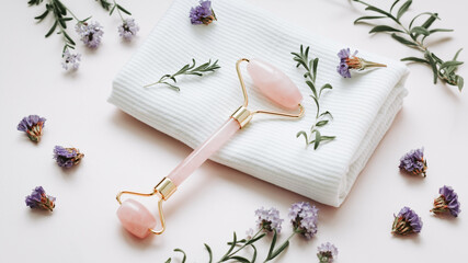 Facial roller with flowers and towel on pink