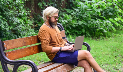 bearded man sit on bench with laptop. online distant education. hipster inspired to work in park. agile business. mature student working on computer. go shopping on cyber monday