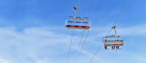 chairlifts one empty and other  transporting people in a winter resort under blur sky