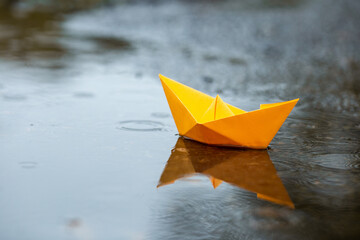 Paper handmade boat toy on a puddle in a rain