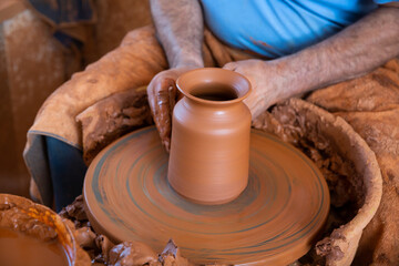 Closeup of skillful male hands creating clay pot on potter wheel
