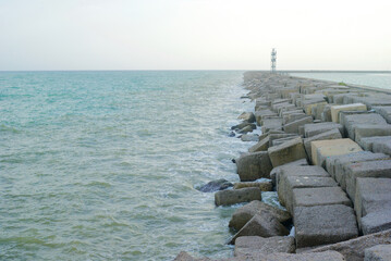 Fototapeta na wymiar sea breakwater rocks and lighthouse in the distance