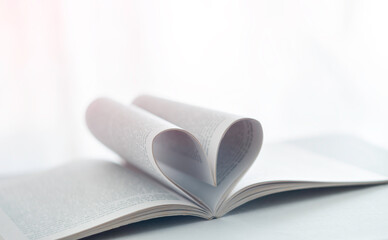 Twisted pages as hear sign. love concept. Soft focus Love story book with open page of literature in heart shape on the white table next to the window. Heart from a book page against the day light.