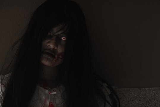 Female zombie in blood. Closeup face and eyes of Asian Woman ghost with blood. Horror creepy scary fear in a dark house. Hair covering the face, Halloween festival concept