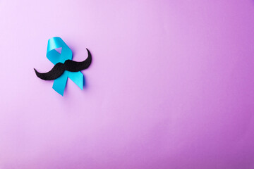 Black mustache paper and light blue ribbon, studio shot isolated on purple background, Prostate cancer awareness month, Fathers day, minimal November moustache concept