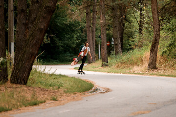 view of road along which young woman rides on skateboard with wakeboard in her hand