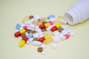 Multicolored pills fall out of a white bottle on a yellow background