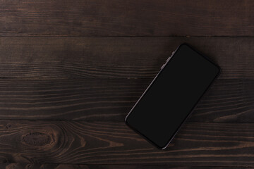 Close up top view of a modern smartphone on black wood table background vintage texture with copy space, mobile phone blank screen display