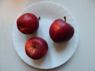 Three fresh red apples on a white plate, top view