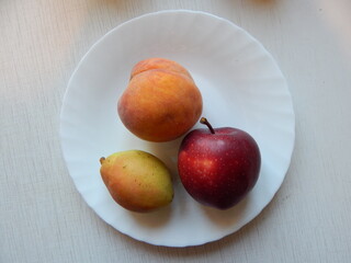 Peach, apple and pear on a white plate, top view