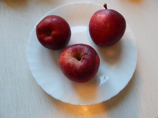 Three fresh red apples on a white plate, top view