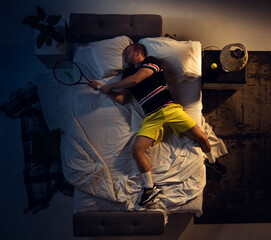 Win. Top view of young professional tennis player sleeping at his bedroom in sportwear with racket. Loving his sport even more than comfort, watching match even if resting. Action, motion, humor.