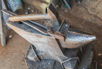 hammer and tongs lie on an anvil in a workshop
