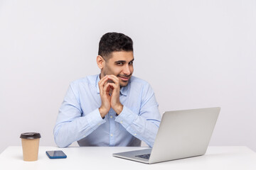 Sneaky scheming businessman sitting office workplace with laptop on desk, clasping hands and...