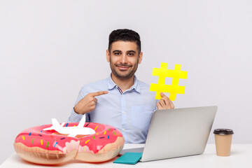 Time to rest! Happy man pointing hashtag symbol, sitting in office workplace with rubber ring...